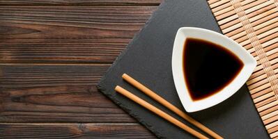 Chopsticks and soy sauce on black stone plate, wooden background with copy space photo