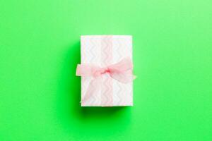 wrapped Christmas or other holiday handmade present in paper with pink ribbon on green background. Present box, decoration of gift on colored table, top view with copy space photo