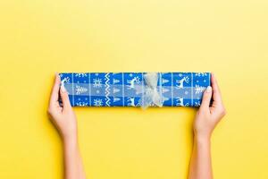 Woman arms holding gift box with colored ribbon on yellow table background, top view and copy space for you design photo