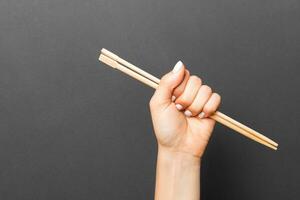 Woman's hand holding chopsticks on black background. Chinese food concept with empty space for your design photo