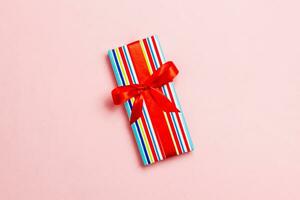 wrapped Christmas or other holiday handmade present in paper with red ribbon on pink background. Present box, decoration of gift on colored table, top view with copy space photo