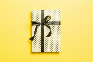 wrapped Christmas or other holiday handmade present in paper with black ribbon on yellow background. Present box, decoration of gift on colored table, top view with copy space photo