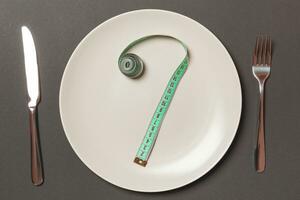 Fork and plate with measuring tape on color background. Diet concept photo