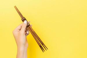 mano femenina sosteniendo palillos sobre fondo amarillo. concepto de sushi con espacio vacío para tu idea foto