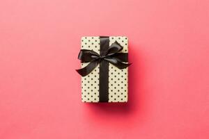 Top view Christmas present box with black bow on living coral background with copy space photo