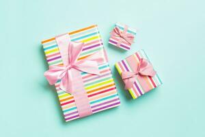 wrapped Christmas or other holiday handmade present in paper with pink ribbon on blue background. Present box, decoration of gift on colored table, top view photo