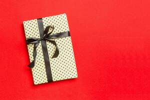 Gift box with black bow for Christmas or New Year day on red background, top view with copy space photo