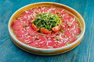 Beef carpaccio with capers, parmesan, arugula and tomatoes photo