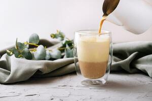 pouring a coffee with milk from teapot to glass cup photo