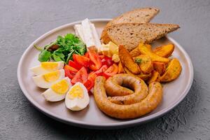 sausages with boiled eggs, tomatoes and potatoes with cheese photo