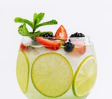 Drink with berries, with lime slices and mint in a wine glass photo