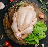 Whole raw chicken on a wooden board with spices for cooking, top view photo