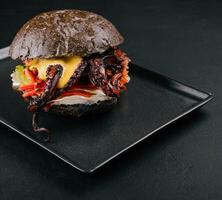 Appetizing marinated octopus burger on a black tray photo