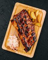 Pork loin ribs served on chopping board and potato wedges photo