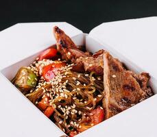 Close-up of noodles in a box with vegetables and beef in teriyaki sauce photo