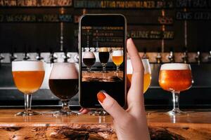 Female hand making a photo of different types of craft beer in glasses