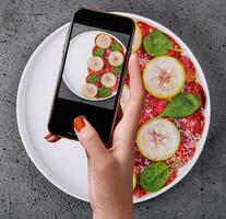 Female hand making a photo of Italian beef carpaccio with sliced zucchini