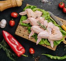 Raw chicken wings with ingredients for cooking on a wooden cutting board photo