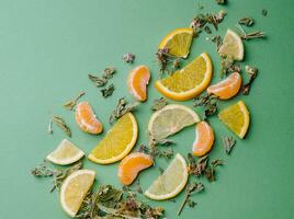 Leaf tea with orange and tangerine slices on green background photo