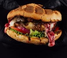 Man holds ready tasty burger in hands in black gloves photo