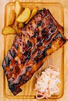 Pork loin ribs served on chopping board and potato wedges photo