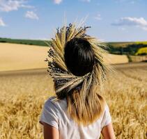 woman in wreath of flowers with wheat and white dress walking along cereal field photo