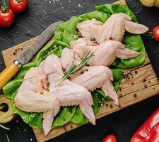 Raw chicken wings with ingredients for cooking on a wooden cutting board over dark stone background photo