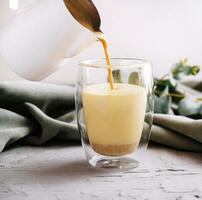 pouring a coffee with milk from teapot to glass cup photo