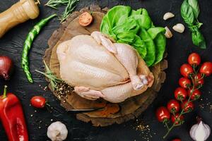 Whole raw chicken on a wooden board with spices for cooking, top view photo