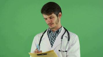 Young male doctor writing on his clipboard on green chromakey video