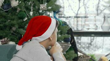 Little boy in Christmas hat looking at the window thoughtfully video