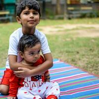 Two happy boys in society park, happy Asian brothers who are smiling happily together. Brothers play outdoors in summer, best friends. Toddler baby boy playing with his happy brother in the garden photo