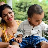 amoroso mamá que lleva de su bebé a hogar balcón. brillante retrato de contento mamá participación niño en su manos. madre con su pequeño 1 año antiguo hijo. foto