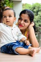 Loving mom carrying of her baby at home balcony. Bright portrait of happy mum holding child in her hands. Mother with her little 1 year old son. photo