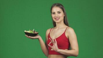 feliz jovem em forma mulher mostrando Está bem placa sorridente segurando uma tigela do fresco salada video
