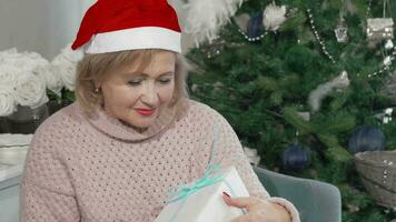 contento mayor mujer en Papa Noel claus sombrero participación fuera un regalo a el cámara video