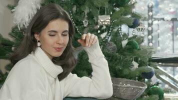 Gorgeous woman smiling to the camera sitting near Christmas tree at home video