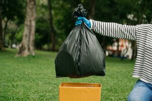 Hand holding garbage black bag putting in to trash to clean. Clearing, pollution, ecology and plastic concept. photo