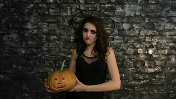 Woman-sorceress holds a pumpkin on black background of a brick wall video
