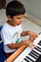 asiático chico jugando el sintetizador o piano. linda pequeño niño aprendizaje cómo a jugar piano. niño manos en el teclado interior. foto