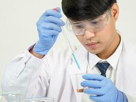 asiático hombre estudiante científico o médico Mira mano participación en reactivo mezcla laboratorio en un Ciencias investigación laboratorio con prueba tubos de varios tamaños en laboratorio química laboratorio blanco antecedentes. foto