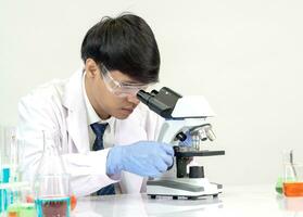 retrato asiático hombre estudiante científico vistiendo un médico vestido en el laboratorio mirando mano a químico. causado por mezcla reactivos en científico investigación laboratorios con prueba tubos y microscopio en el mesa foto