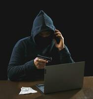 Hacker spy man one person in black hoodie sitting on a table looking computer laptop used login password attack security to circulate data digital in internet network system, night dark background. photo