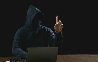 Portrait hacker spy man one person in black hoodie sitting on table looking computer laptop used login password attack security to data digital internet network system night dark background copy space photo