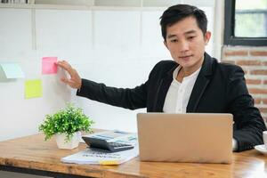 Serious businessman managing project tasks on sticky notes writes start-up business ideas using colorful Post-it stickers, plans corporate strategy board. Creative priority to-do list concept. photo