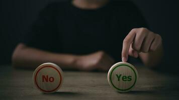 Close up image of man's hand putting wooden dice with yes and no signs photo