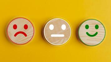 Concept of customer satisfaction. Happy sad and neutral smile faces on wooden blocks on a yellow background. Customer satisfaction, evaluation, or feedback concept. photo