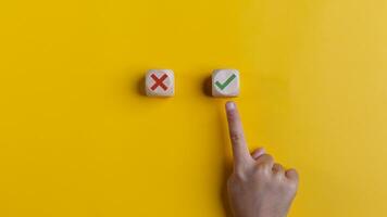 Right and wrong icons on wooden cubes with hand choosing the right icon on yellow background. Approving, voting, or right decision concept. photo