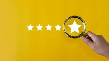 Hand holding a magnifying glass with a five-star rating on a yellow background. feedback review satisfaction service, Customer service experience, and business satisfaction survey. photo