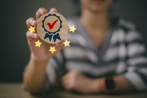 Woman hand holding the sign of the top service Quality assurance 5 star, on a wooden background. Guarantee, Standards, ISO certification, and standardization concept. photo